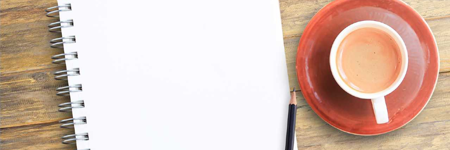 a notepad and pencil on a wooden table next to a cup of coffee on a saucer